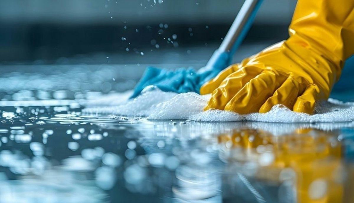 Gloved hand scrubbing a floor with soapy water during a deep clean