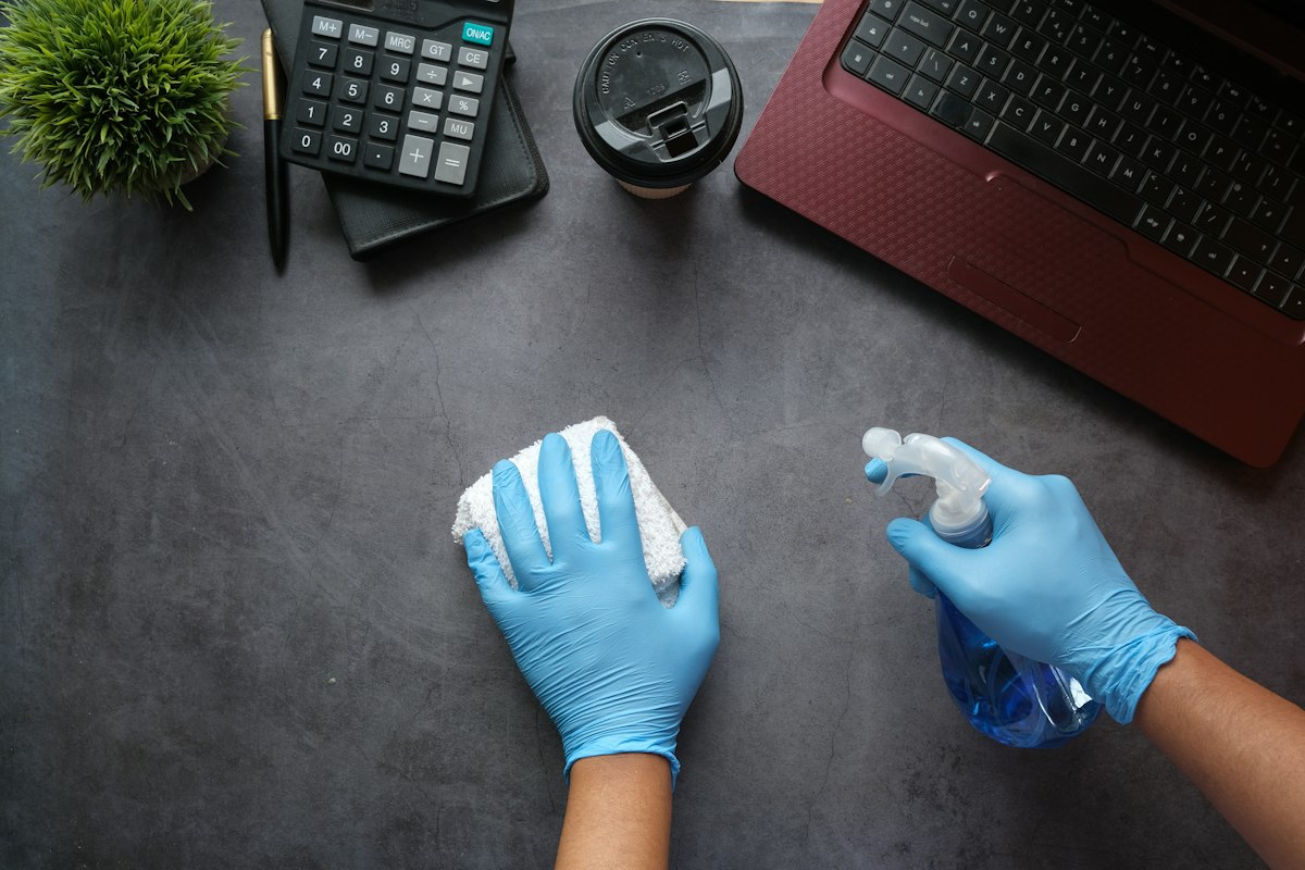 Gloved hands disinfecting an office desk