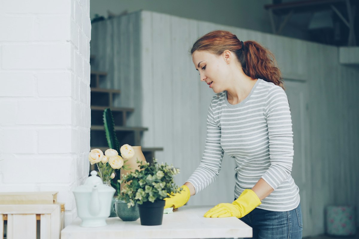 Housekeeper in yellow gloves wiping down a dining table