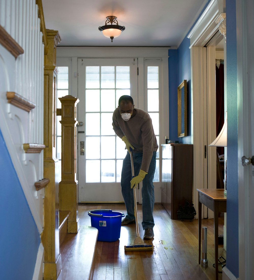 Cleaner in a dust mask mopping hardwood floors after a home renovation